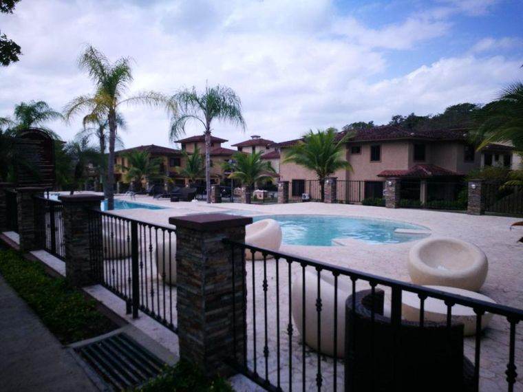 Piscina con asientos redondos y camastros, con edificios residenciales de techo de teja al fondo
