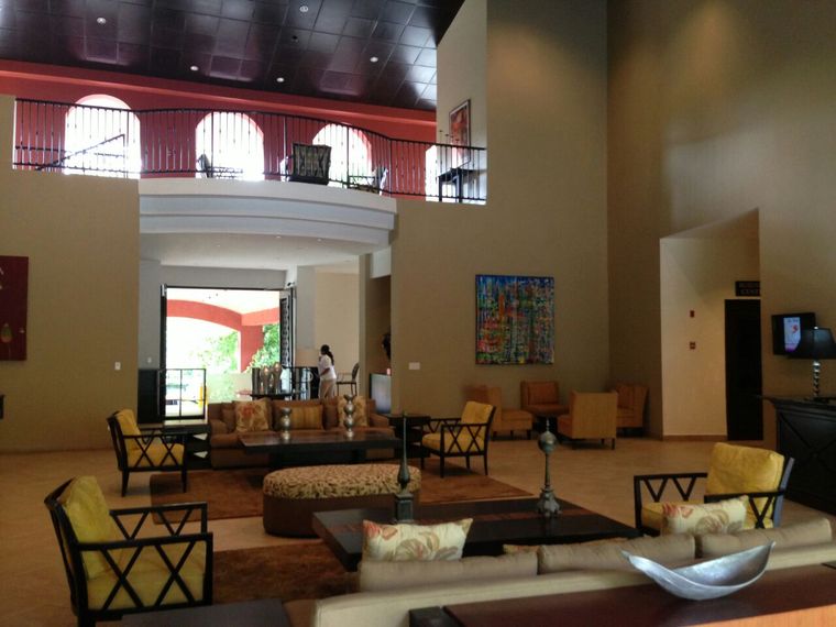 Salón social de doble altura con sofás, sillones y balcón interior con arcos