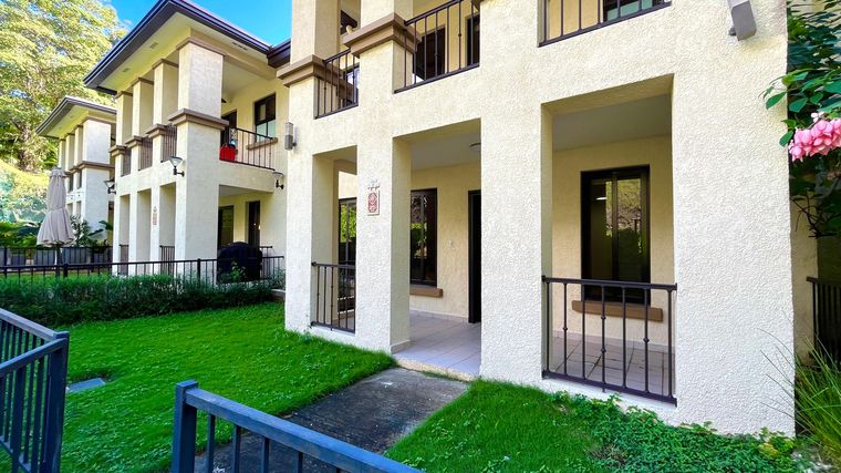 Townhome de fachada clara con portal techado, barandas de hierro y jardín